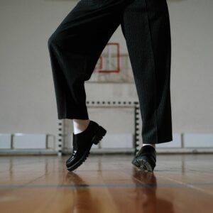 Stylish black leather shoes and pants in a gym setting with wooden flooring.